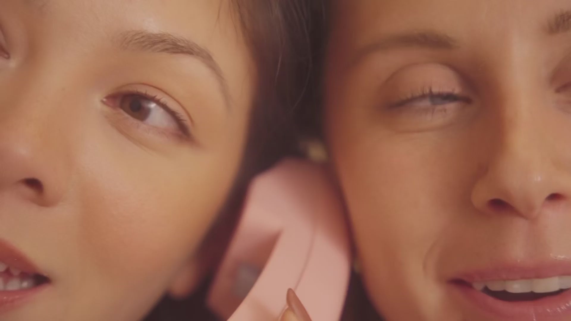 two friends listening on one phone handset with their faces pressed close together