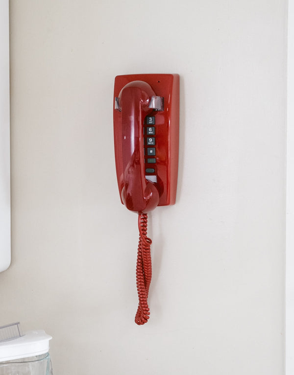 Red wall phone mounted on a white wall